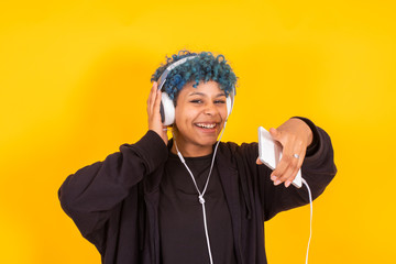 young afro american girl with mobile phone and headphones dancing isolated on yellow background in casual urban style