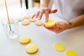 A woman's hands decorating cookies with yellow fondant