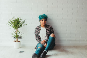 trendy young girl at home or apartment on the floor with plant and white brick background
