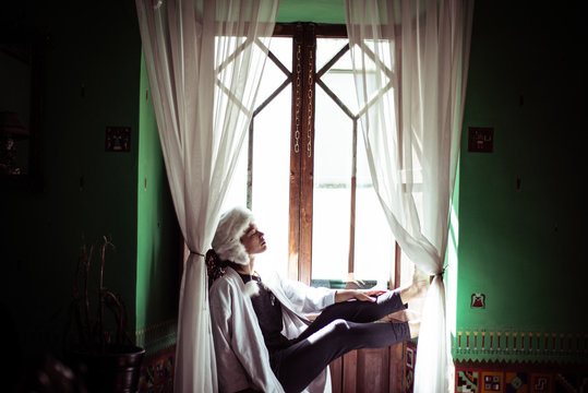 Androgynous woman in alpaca hat sits in window of Spanish colonial fla