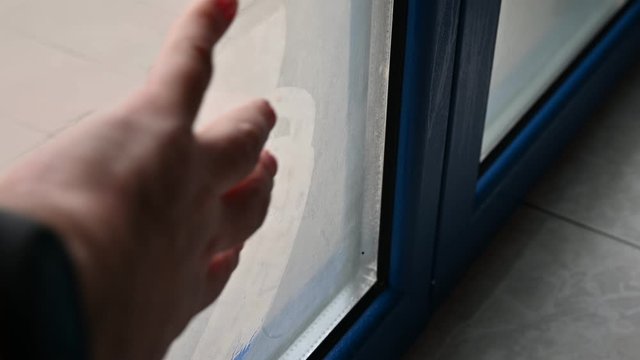 The problems of thermal insulation cause condensation on the window frame: the Caucasian man's hand passes over the fogged glass, highlighting the formation of humidity.