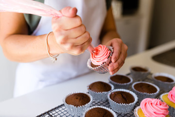 A cupcake being frosted with pink icing