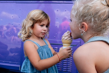 Happy pair of sisters sharing and licking ice cream cone