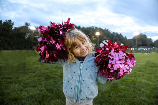 little girl smiling holding pompoms at football game at dust
