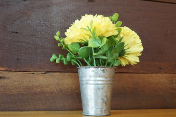 Yellow flowers with green leaves in an aluminum flower pot.