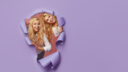 Surprised young women stands in torn paper hole, has excited cheerful expression, looks through breakthrough of purple background. Wow, great news. Mockup, space for text