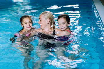 Mother with two daughters having fun in indoor swimming-pool. Girl is resting at the water park. Active happy kid. Swimming school for small children. Concept friendly family sport  summer vacation.