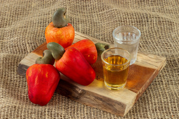 Red cashew fruit with raw cashews nut. In a piece of wood, with two shots of cachaca. One is aged in a oak barrel.  With old bag background. 
