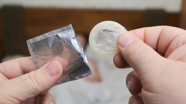 concept of safe sex between man and woman, contraception. man takes out condom when woman lies in bed in bedroom.