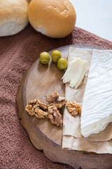 vertical photo, brie cheese with nuts and olives lies on a wooden board near freshly rolled buns