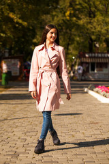 Portrait of a young brunette girl in pink coat on a background of autumn park