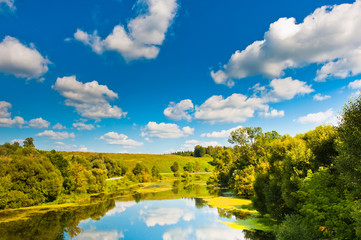 Forest, river and blue sky with big white clouds in sunny summer day