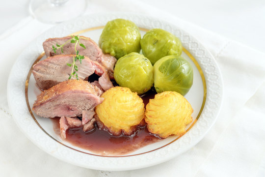Tenderly roasted duck breast fillet with brussels sprout and duchess potatoes on a white plate, a festive dinner for holidays
