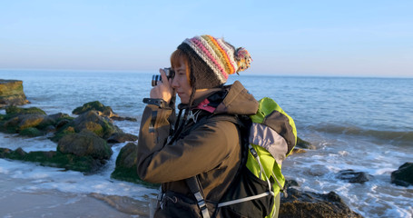 Young female travelr with backpack and retro film camera travel in the autumn mountains near sea	
