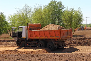 Obraz premium Heavy sand load dumper truck on ground construction site on Sunny summer day, bulk cargo transportation