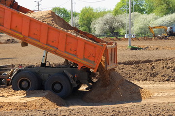 Heavy yellow tipper truck unloading sand from dump bed on construction site on Sunny summer day © Ilya
