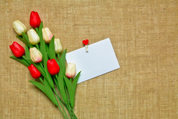Bunch of tulips with a note sheet and heart paper pin on the hessian background. Women's Day Mother's day concept