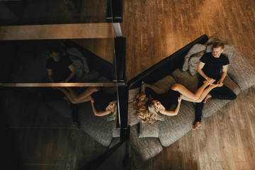 A young attractive man and a pregnant woman with blond hair sit in a room with a fashionable loft design.