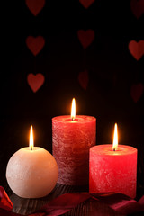 Three wax flame candlelight with ribbon in dark romantic light on hearts background, love dating, Valentine's day
