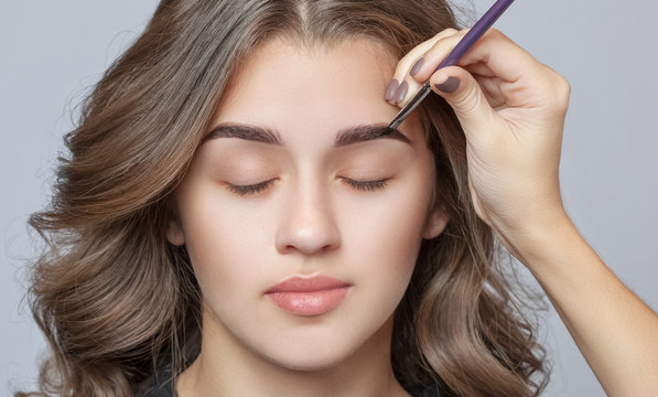 Make-up artist does eyebrow make-up to a woman with curly brown hair and nude make-up. Beautiful thick eyebrows close up. Professional makeup and cosmetology skin care.