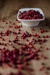 Red peppercorns in white bowl on wooden background