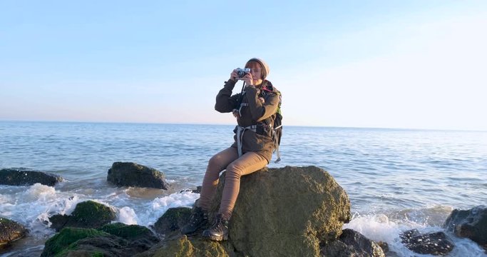 Young female travelr with backpack and retro film camera travel in the autumn mountains near sea
