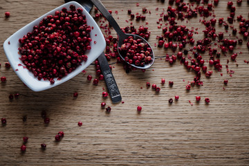 Red peppercorns in white bowl on wooden background