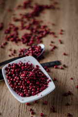 Red peppercorns in white bowl on wooden background