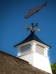 A weather vane on top of a New England house uses the cardinal points of the compass and a tuna to show which way the wind is blowing in Maine.