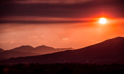 Fototapeta premium Smoke and clouds from burning wildfires casts ominous shadows in the sky at sunset.