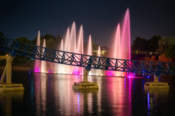 Large multi colored fountains reflected in the water during night show.