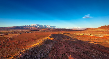 Fototapeta na wymiar Red dirt and red rocks catch the light of a setting sun as rare snow caps distant rock and mountains in Southern Utah not far from St. George.