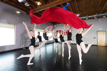 Group of young ballet dancers playing and having fun in dance studio with colorful fabric