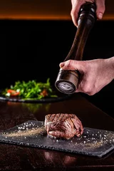 Rolgordijnen American cuisine. Chef season salt on a juicy beef steak in a restaurant. background image, copy space © zukamilov