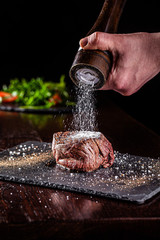 Obraz na płótnie Canvas American cuisine. Chef season salt on a juicy beef steak in a restaurant. background image, copy space