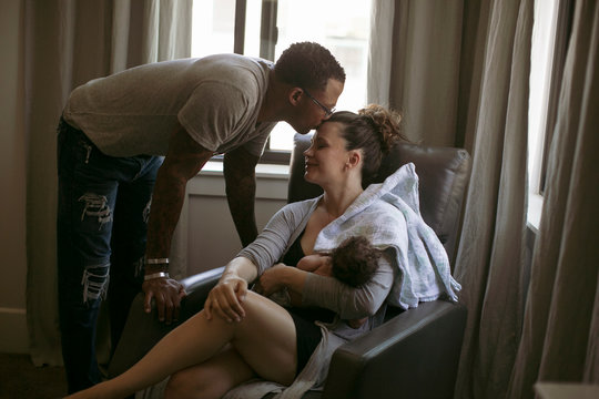 Loving man kissing woman's forehead with baby girl at home