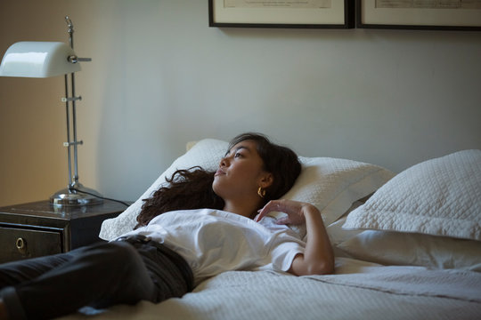 Thoughtful woman looking away while lying on bed at home