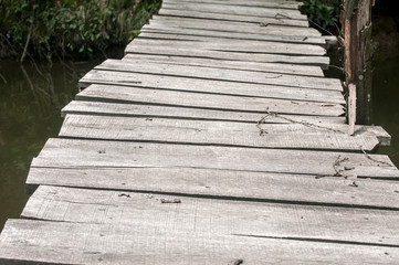 Small weathered wooden boards bridge over river waters closeup