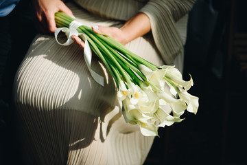 Woman in pastel or ivory dress holding a beautiful bouquet of calla lily flowers