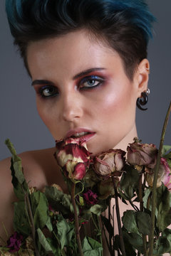 Studio portrait of a beautiful girl with blue hair and a fashion make-up without clothing with bouquet of flowers. Fashion style