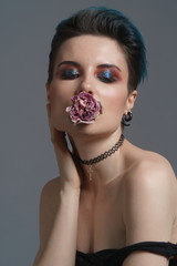 Studio portrait of a beautiful girl with blue hair and a fashion make-up in a little black dress with a rose in her mouth. Fashion style