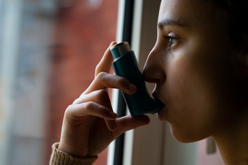 Young woman taking the blue asthma inhaler to treat an asthma attack. - obrazy, fototapety, plakaty