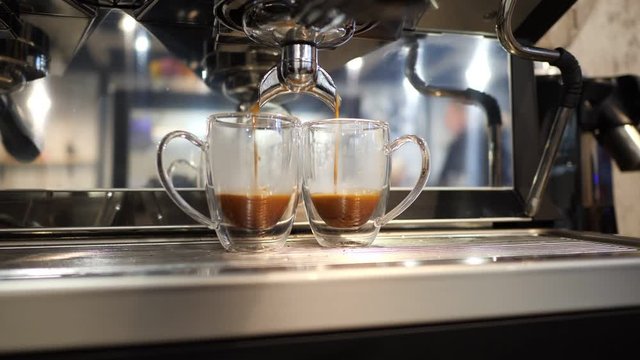 Strong espresso coffee comes out of coffee machines and goes into two glass cups