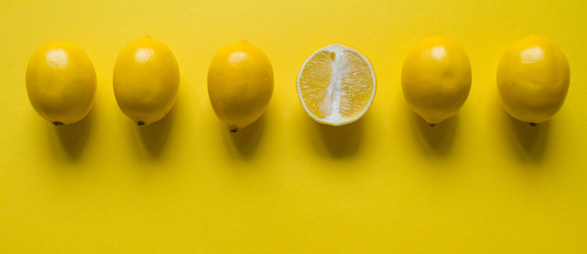 Top view whole and sliced ripe lemon slaid out in a row on a yellow surface, concept of health and vitamins