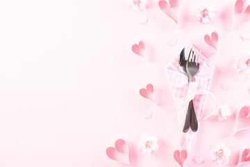 Pink paper hearts with table set with set of silverware fork and spoon on Light pink pastel paper background. Love and Valentine's day concept.