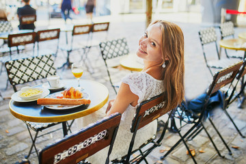 Cheerful young woman having breakfast or brunch in traditional French cafe