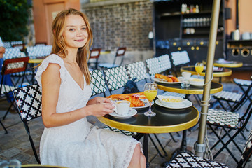 Cheerful young woman having breakfast or brunch in traditional French cafe