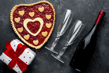 heart-shaped cake with jam, a bottle of wine and glasses and a gift with a red ribbon, on a stone background with copy space for your text. valentine's day celebration concept
