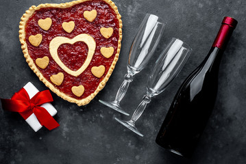 heart-shaped cake with jam, a bottle of wine and glasses and a gift with a red ribbon, on a stone background with copy space for your text. valentine's day celebration concept