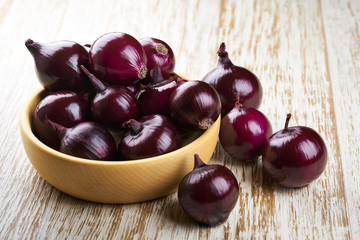 Red onions in wooden bowl on wooden table selective focus.